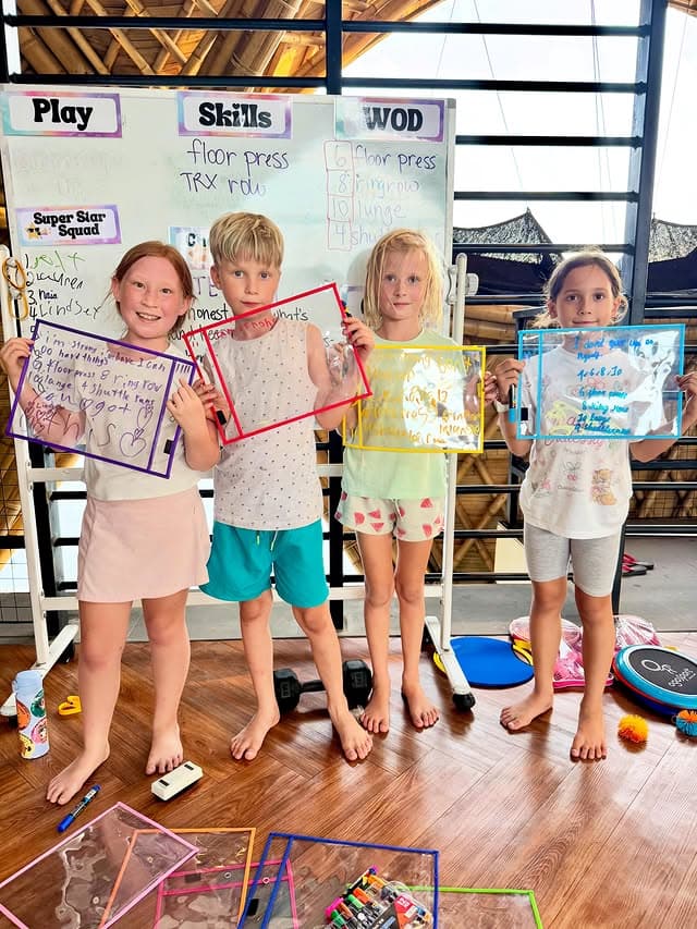 Four children at a Kaizen Kids class holding up the goals and mantras they wrote